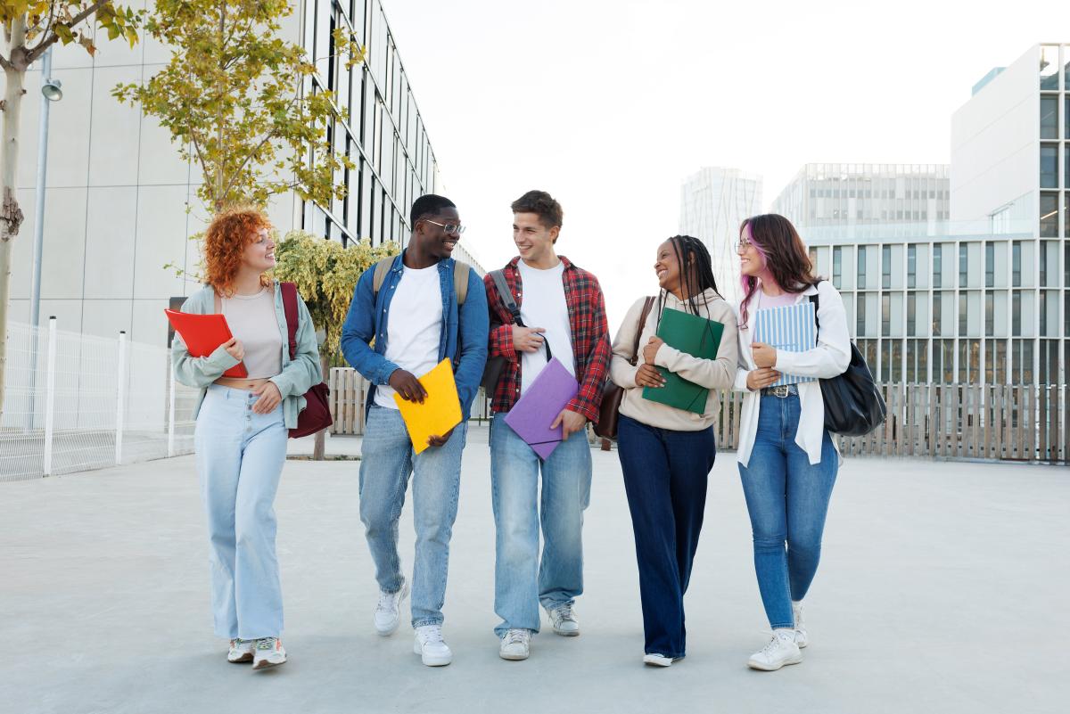 Diverse Gruppe mit fünf jungen Erwachsenen spaziert lachend über Campus
