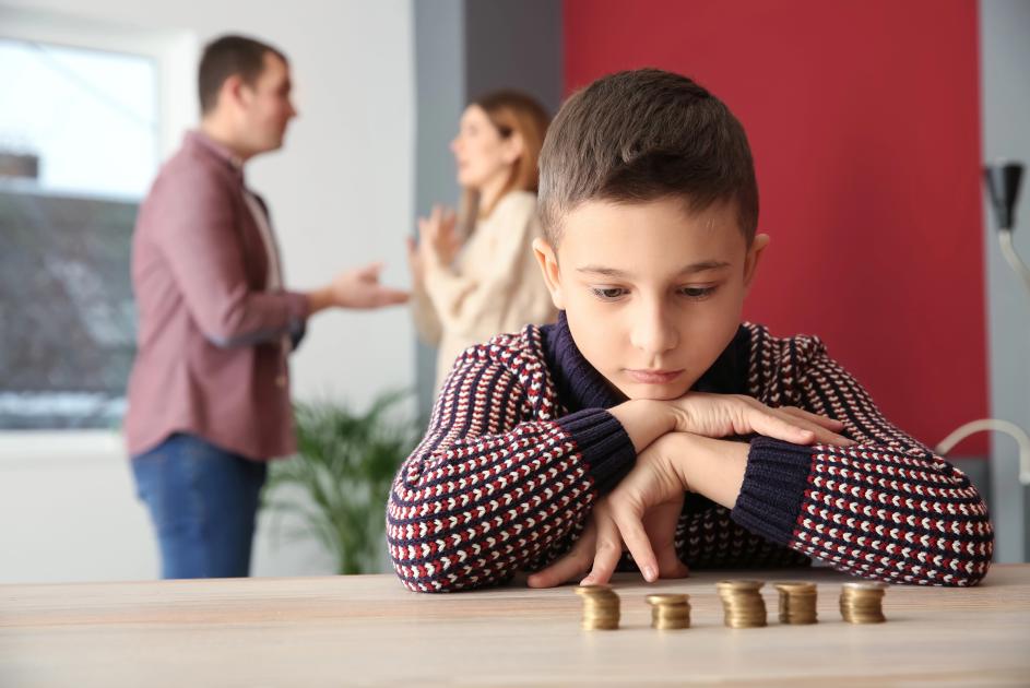 Kind zählt Geld, im Hintergrund streiten die Eltern