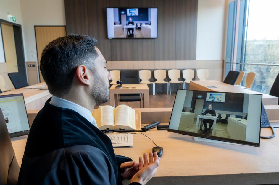 Mann in Robe im Gerichtssaal vor Bildschirm